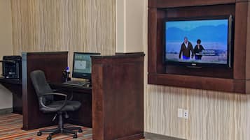 A hotel room with a desk, computer, and a television mounted on the wall.