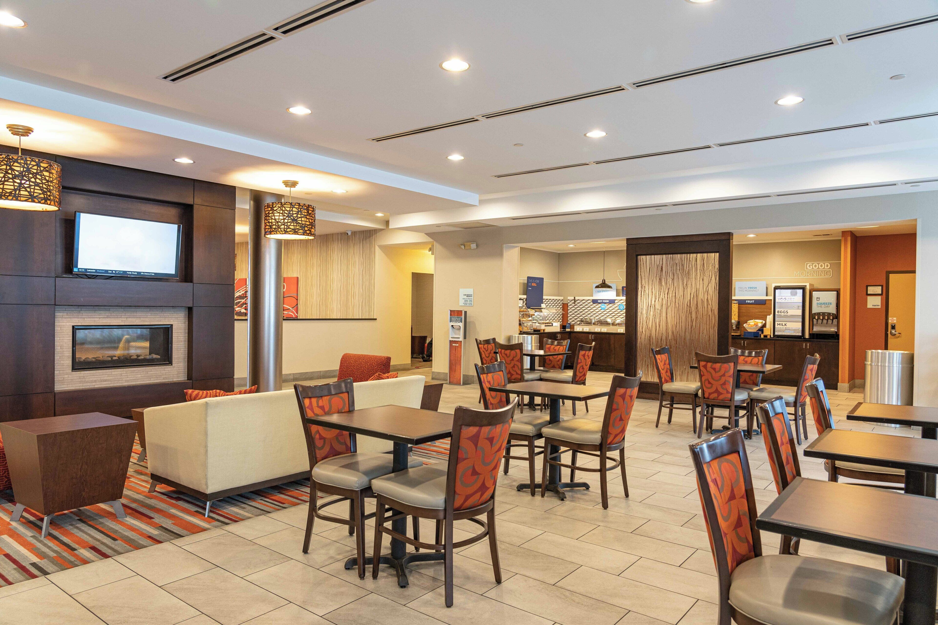 A hotel lobby with seating areas, a TV screen, and a food counter.