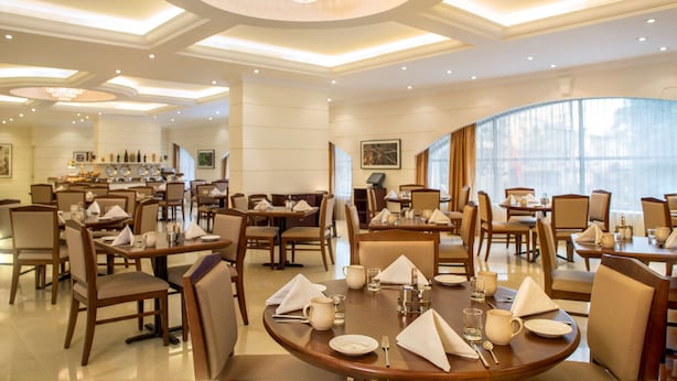 Une salle à manger spacieuse, avec de nombreuses tables dressées, de magnifiques lustres et une vue sur la ville grâce à de grandes fenêtres.