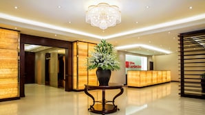 Un hall d’hôtel avec un comptoir d’accueil, un lustre et une plante en pot.