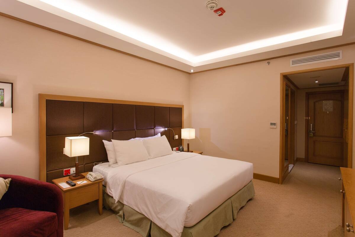 A hotel room with a large bed, two bedside tables, a red chair, and a wooden door.