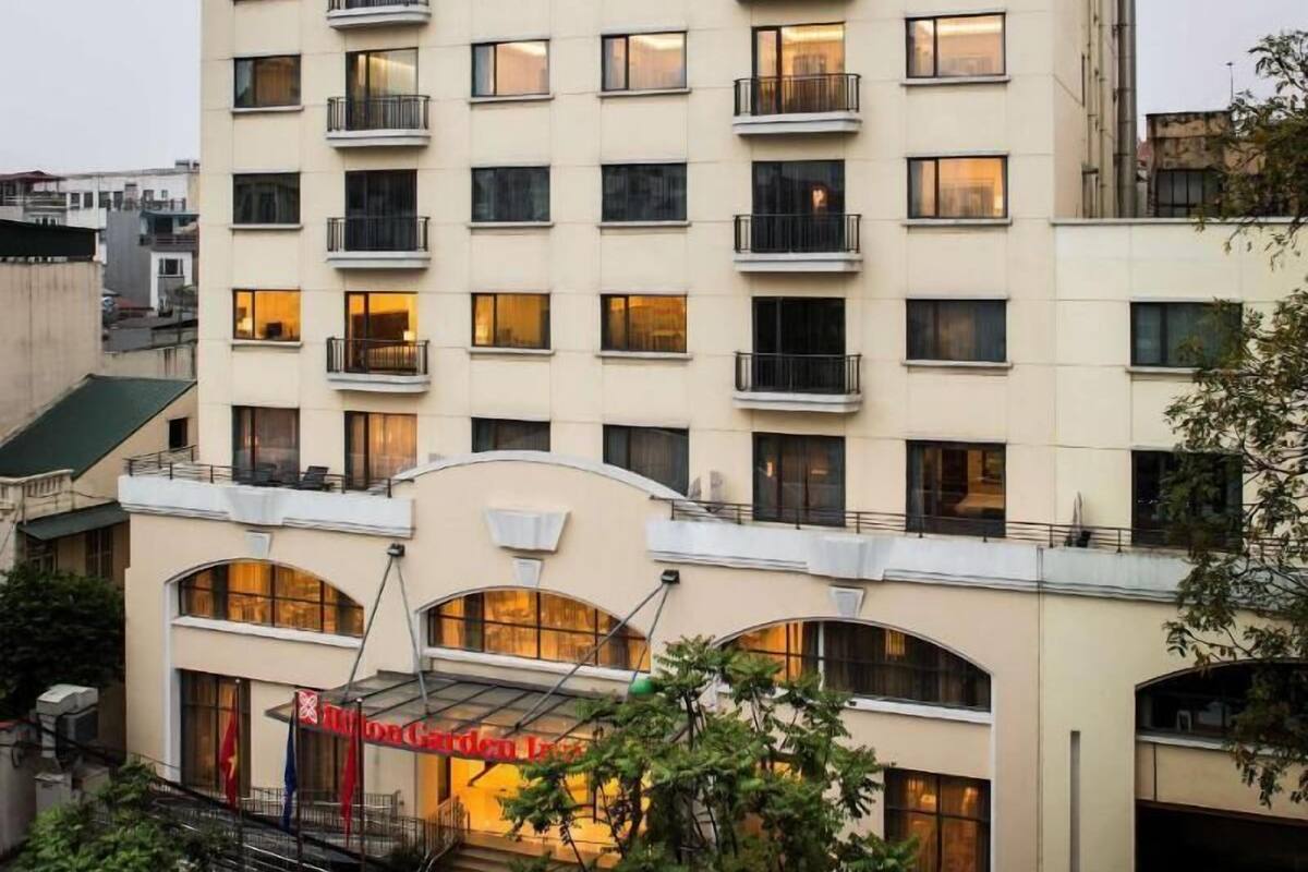 A multi-story hotel with a prominent 'Hilton Garden Inn' sign, a central entrance with a glass canopy, and balconies on each floor.