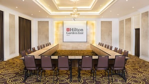 Une salle de conférence équipée d’une longue table, de chaises et d’un grand écran affichant le logo de l’hôtel Hilton Garden Inn.