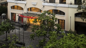 Un hôtel reconnaissable à son grand panneau rouge, son entrée abritée et son escalier menant à l’entrée.
