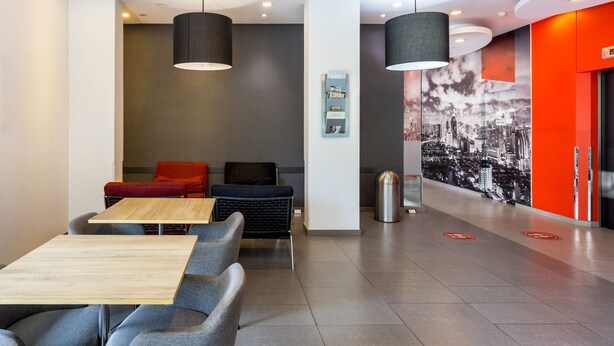 A modern hotel lobby with a seating area, a wooden table, and a cityscape mural. - Easy Planet Bangkok Asoke (Bangkok)