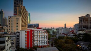 A cityscape with various buildings, including a prominent red and white building with multiple floors and a large window structure in the background. - Easy Planet Bangkok Asoke (Bangkok)