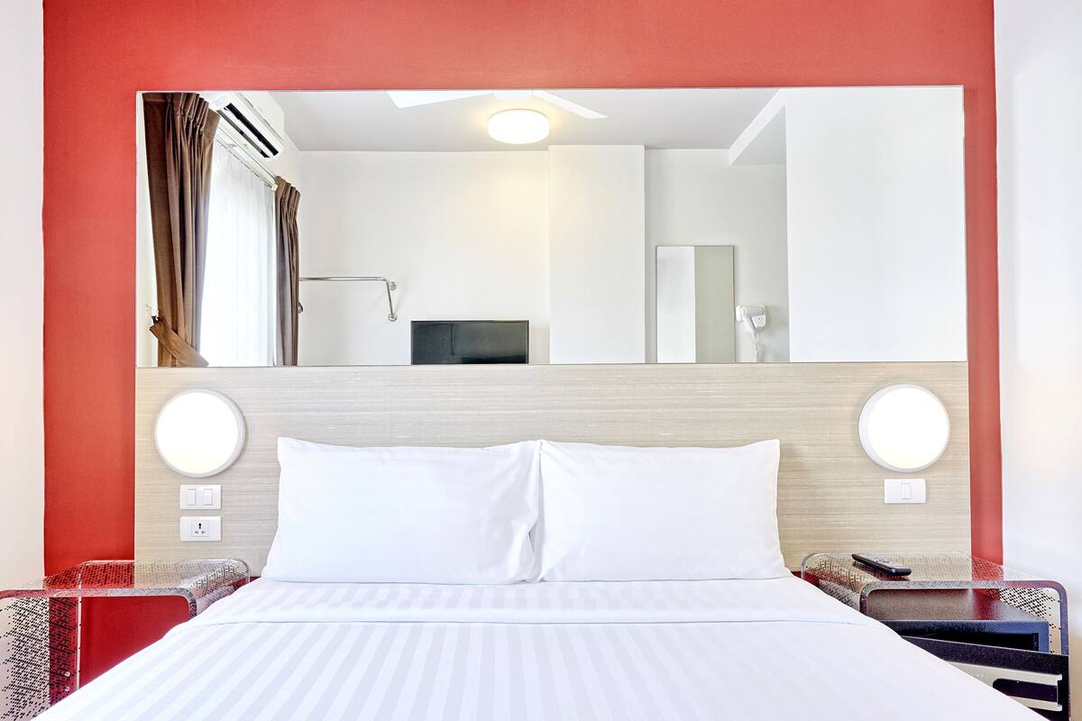 A hotel room with a large bed, a mirror above the bed, and a red accent wall.
