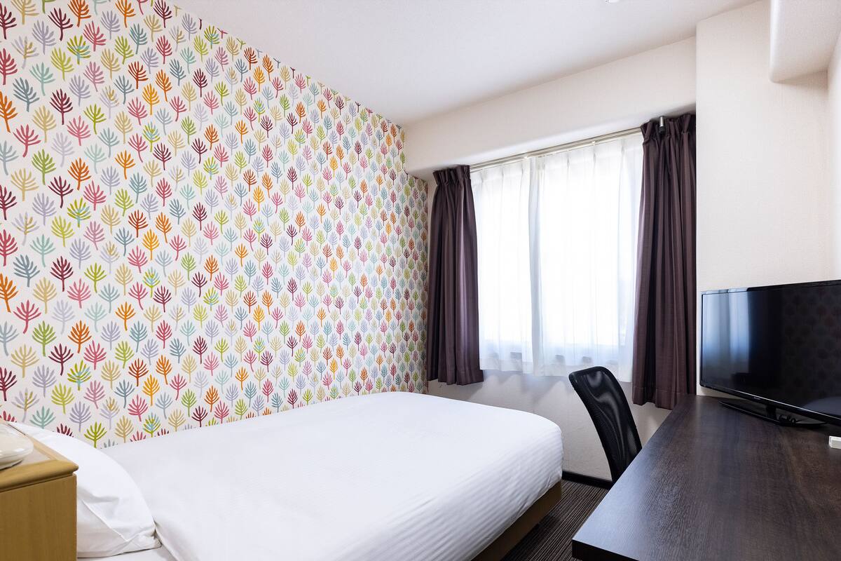 A hotel room with a bed, a desk, a TV, and a window with curtains.
