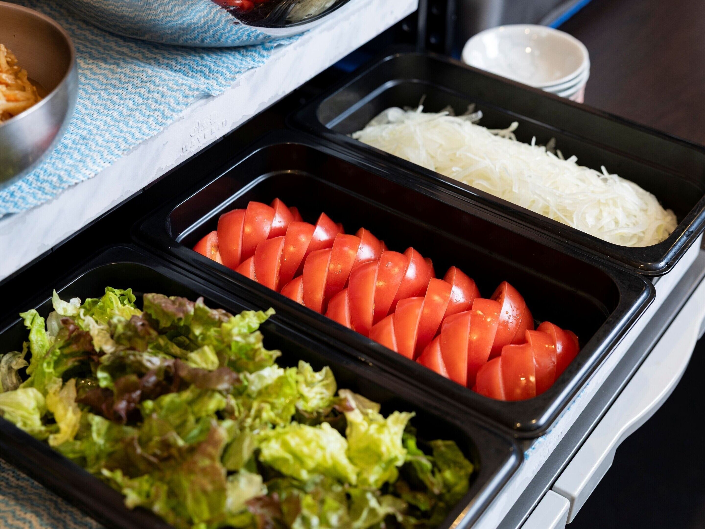 Un buffet proposant des tomates en tranches, du chou râpé et un mélange de jeunes pousses.