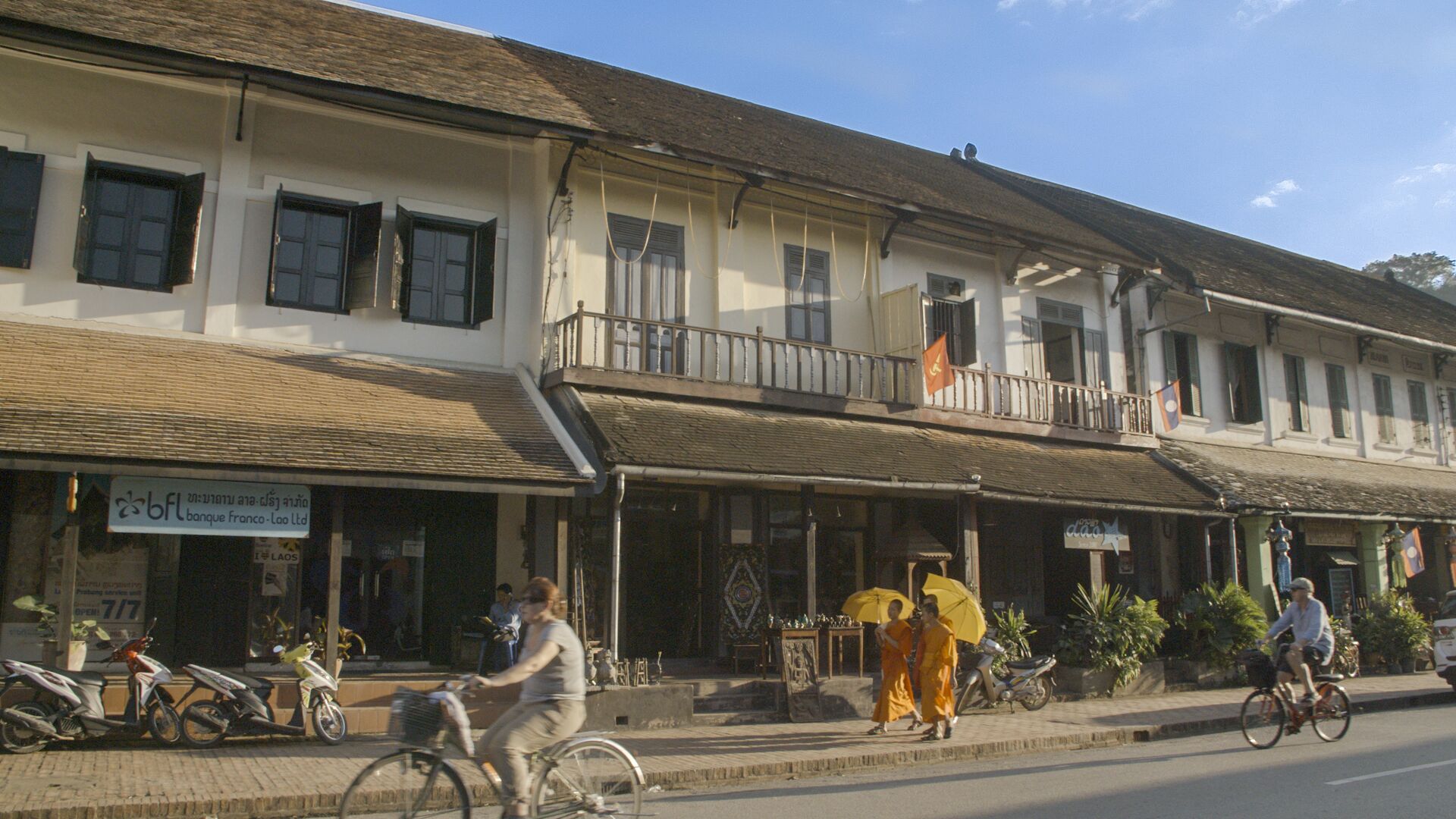 A building with a balcony, a sign for 'bfl bank', and a street with people and bicycles.