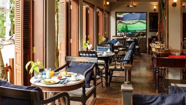 A restaurant with wooden shutters, tables with chairs, and a television screen in the background. - Burasari Heritage Luang Prabang (Luang Prabang)