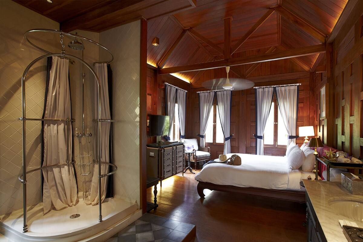 Un dormitorio amplio con una cama grande, techo de madera y zona de ducha con cortinas.