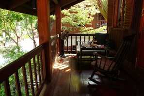 A wooden porch with a table and chairs, a rocking chair, and a fan. - Burasari Heritage Luang Prabang (Luang Prabang)