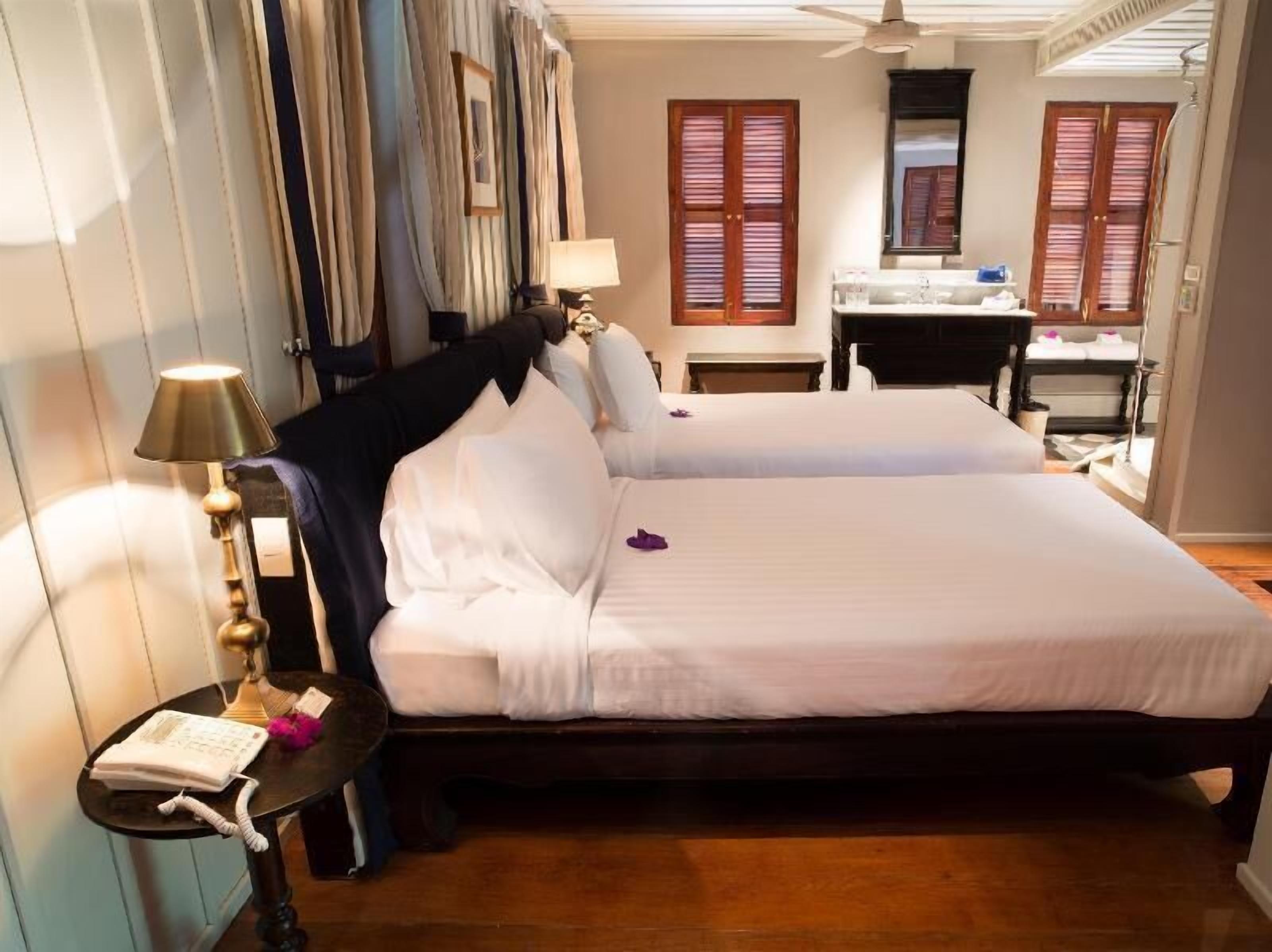 A hotel room with a double bed, a bedside table with a lamp, a desk with a chair, and a mirror.