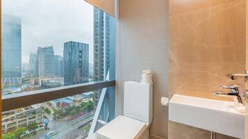 A modern bathroom with a toilet, sink, and a large window offering a city view.