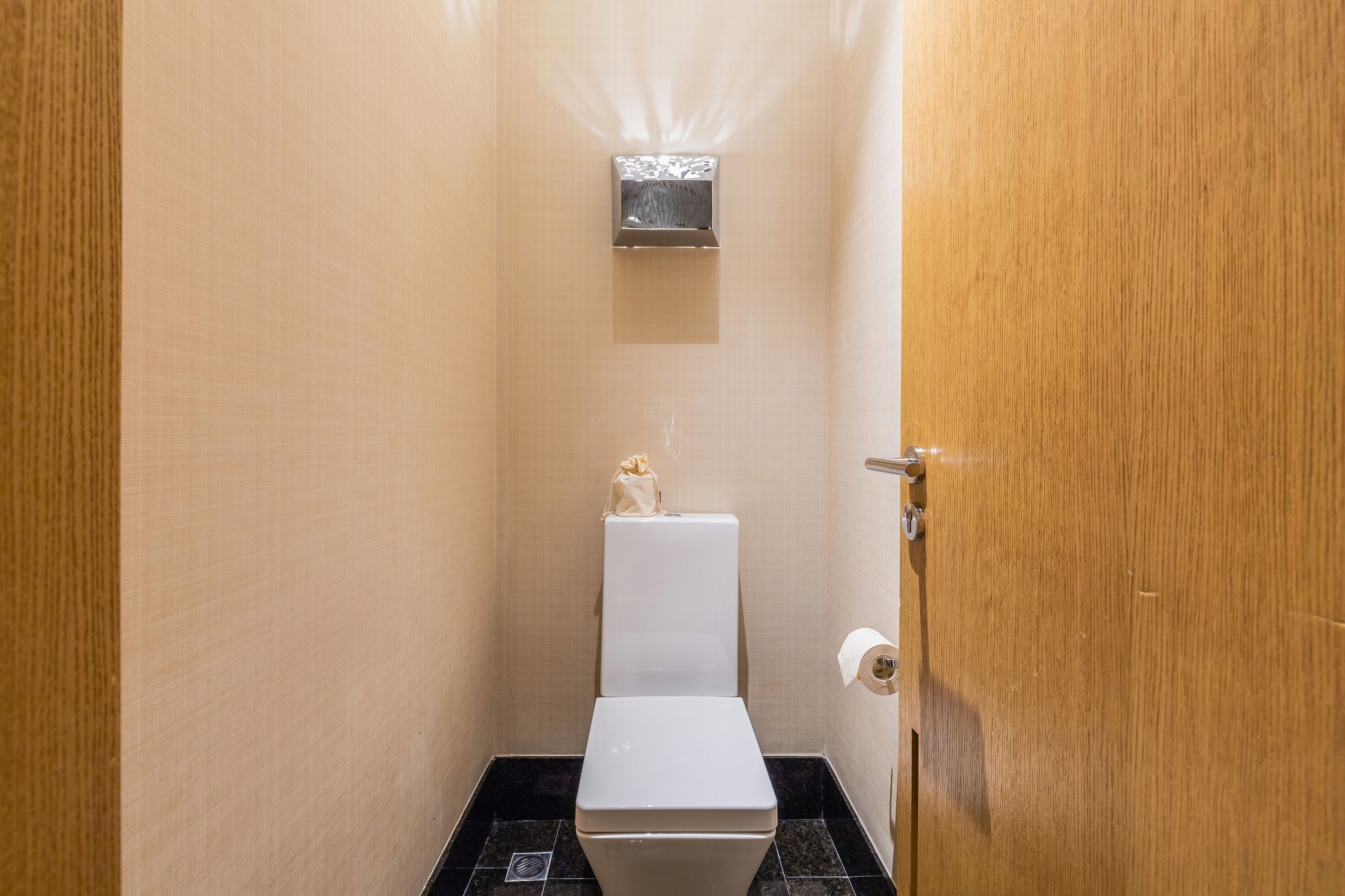 Ein kleines, schmales Badezimmer mit einer weißen Toilette, einem an der Wand befestigten Bidet und einer Holztür.