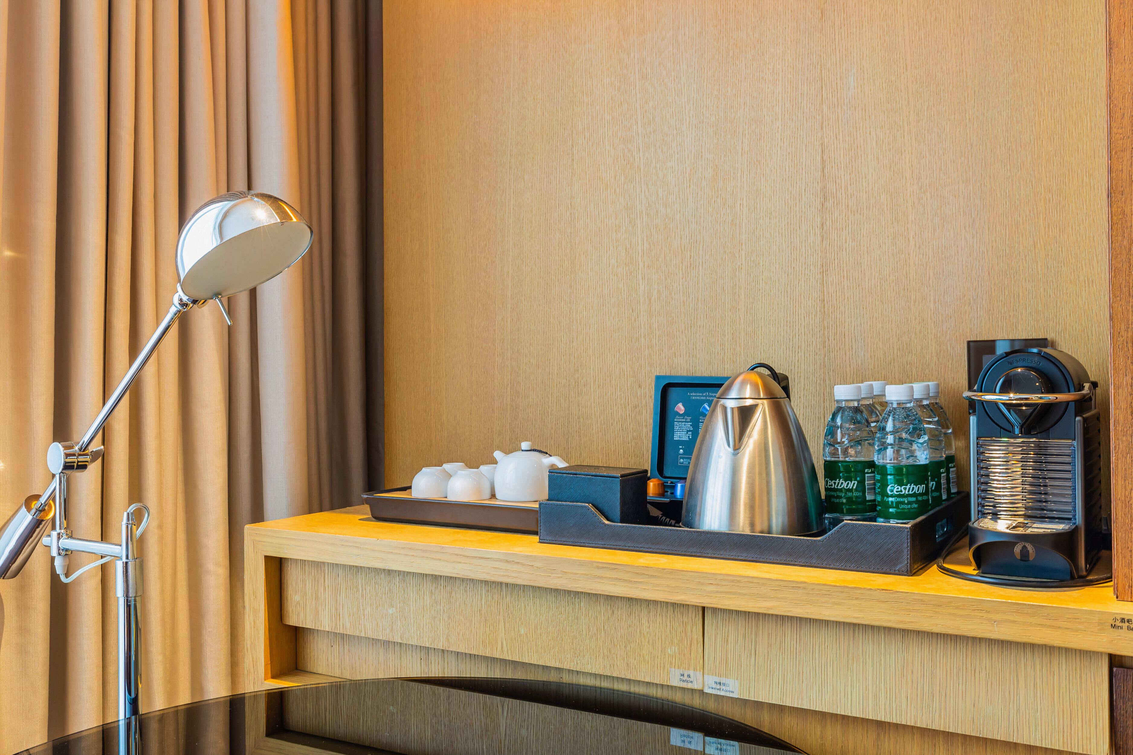 A hotel reception area with a desk, a coffee machine, a kettle, and a tray with teapots and bottled water.