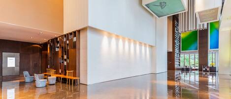 A spacious lobby with a polished marble floor, seating areas, and a large staircase leading to upper levels.