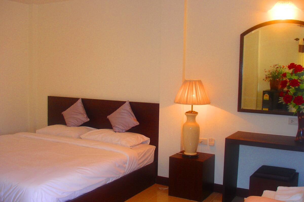 A hotel room with a bed, a nightstand with a lamp, a mirror, and a vase with flowers.