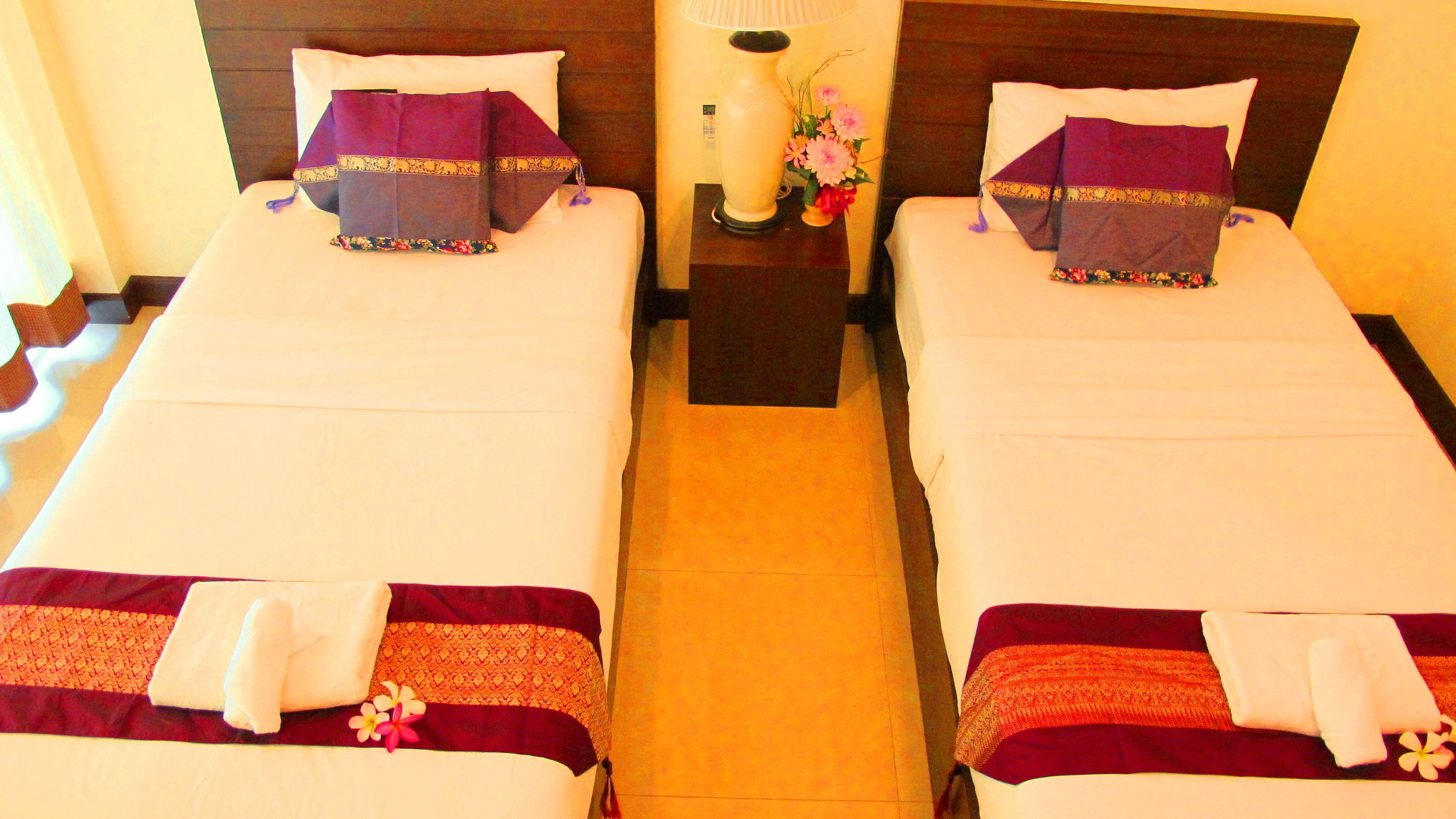 Two twin beds with matching headboards, a nightstand with a lamp and flowers, and a decorative vase.