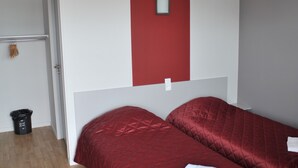 A room with two beds, a red accent wall, a white ceiling, and a wooden floor.