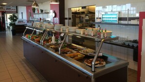 A buffet area with multiple food stations, a kitchen in the background, and a sign for 'Le Bistro Relais'.