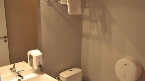 A bathroom with a white sink, a toilet, and a towel dispenser.