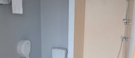 A bathroom with a toilet, a hand dryer, a towel rack, and a shower area.