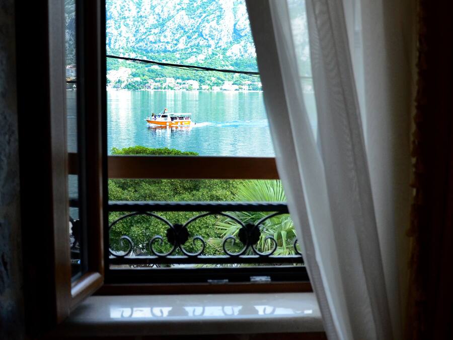 Ein Fenster mit Blick auf einen See und ein Boot, Vorhänge sind teilweise zugezogen, und ein Balkongeländer.