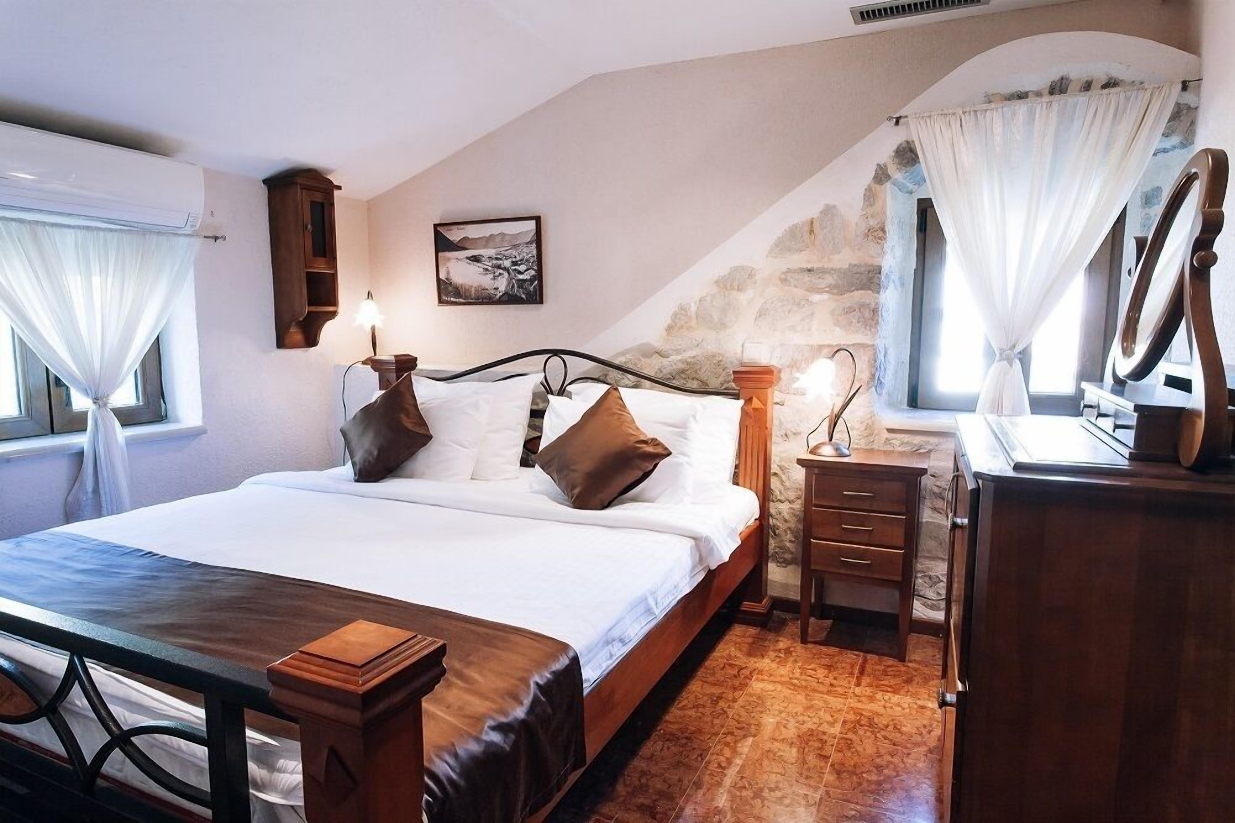 A bedroom with a bed, bedside table, dresser, and a stone wall.