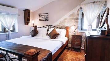 A bedroom with a bed, bedside table, dresser, and a stone wall.