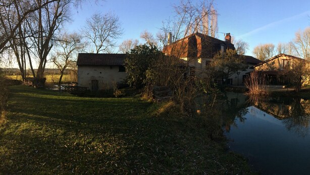 Un entorno tranquilo junto al lago con edificios tradicionales, cielo despejado y una masa de agua calma que refleja las construcciones.