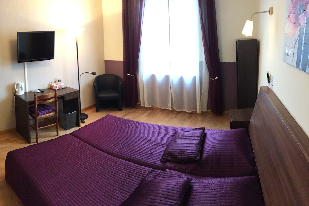 Habitación de hotel con una cama grande, un escritorio con una silla, un televisor y una ventana con cortinas.