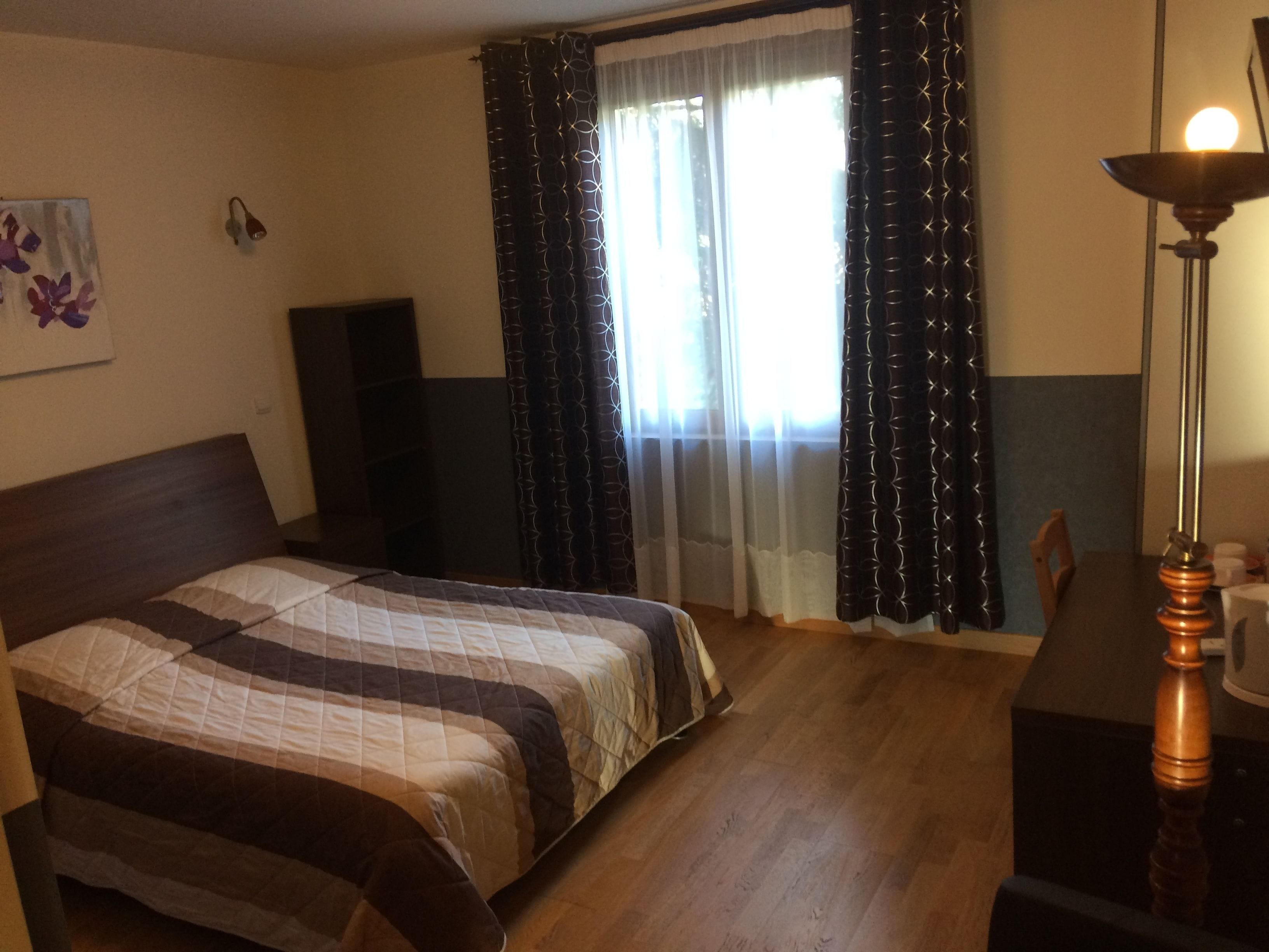A bedroom with a bed, a desk, a lamp, and a window with curtains.