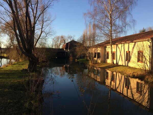 A riverside building with a traditional architectural style, featuring a tiled roof and a reflection in the water.