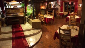 Un restaurante con un piano, varias mesas con manteles rojos y un suelo de baldosas.