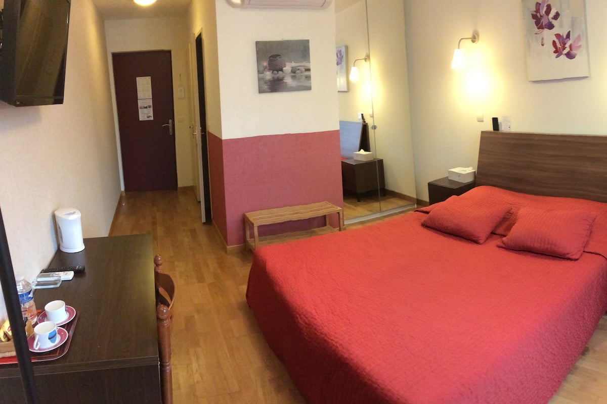 Habitación de hotel con una cama grande, mesitas de noche, un escritorio con una silla, un espejo y una puerta.
