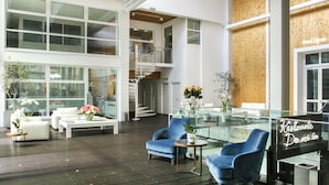 Un hall d’entrée spacieux au design moderne, avec une table basse en verre, des fauteuils bleus, des canapés blancs et un escalier menant à un niveau supérieur.