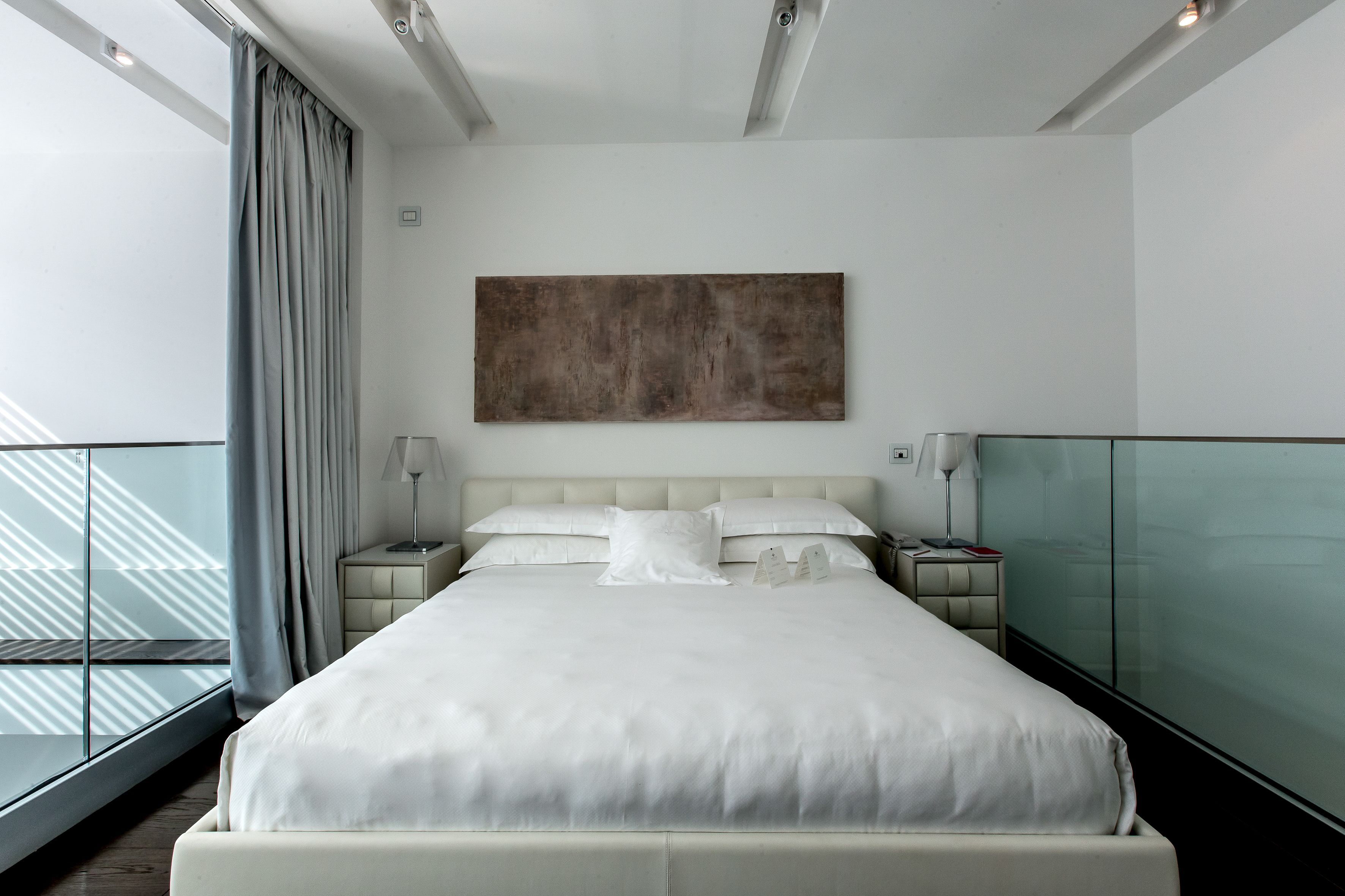 Camera d'albergo moderna con un letto grande, un divisorio in vetro e vista sul cielo.