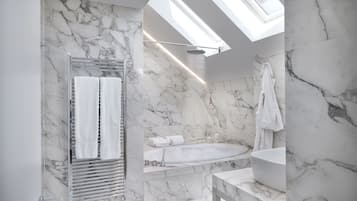 A modern bathroom with a skylight, a glass-enclosed shower, and a marble-tiled sink.