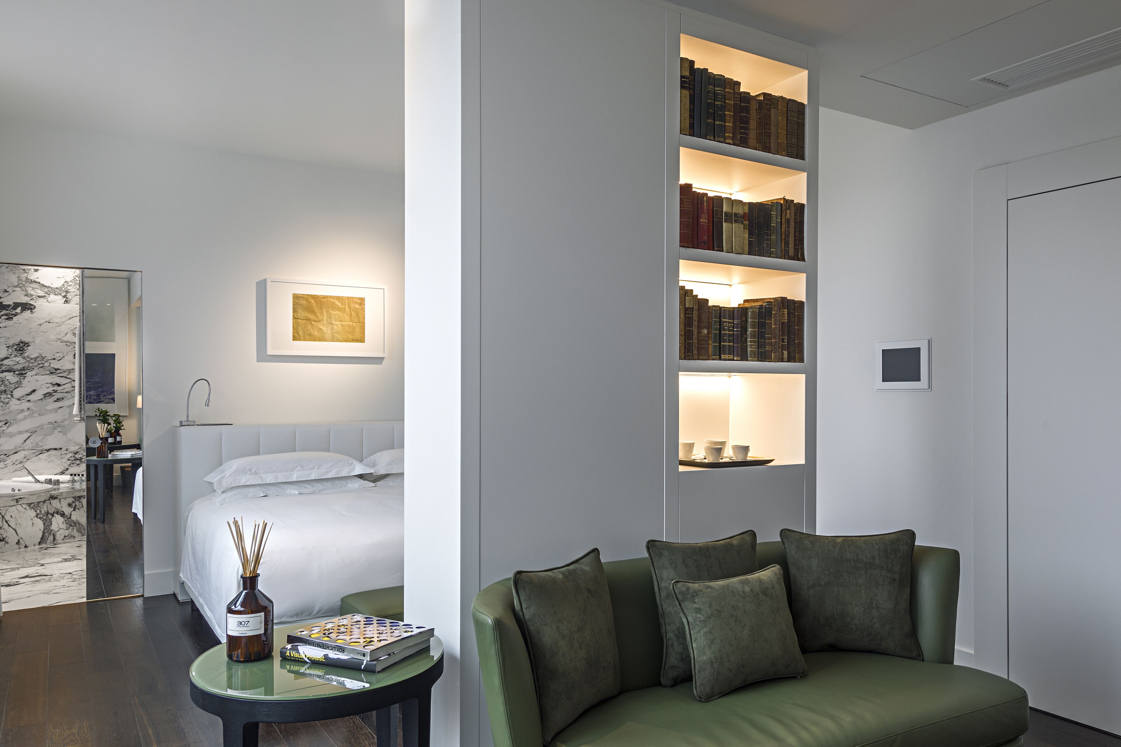 Una habitación de hotel moderna con una cama, un sofá verde, una estantería y una pared de mármol.