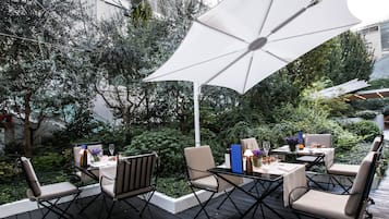 Un patio al aire libre con mesas y sillas, rodeado de abundante follaje.