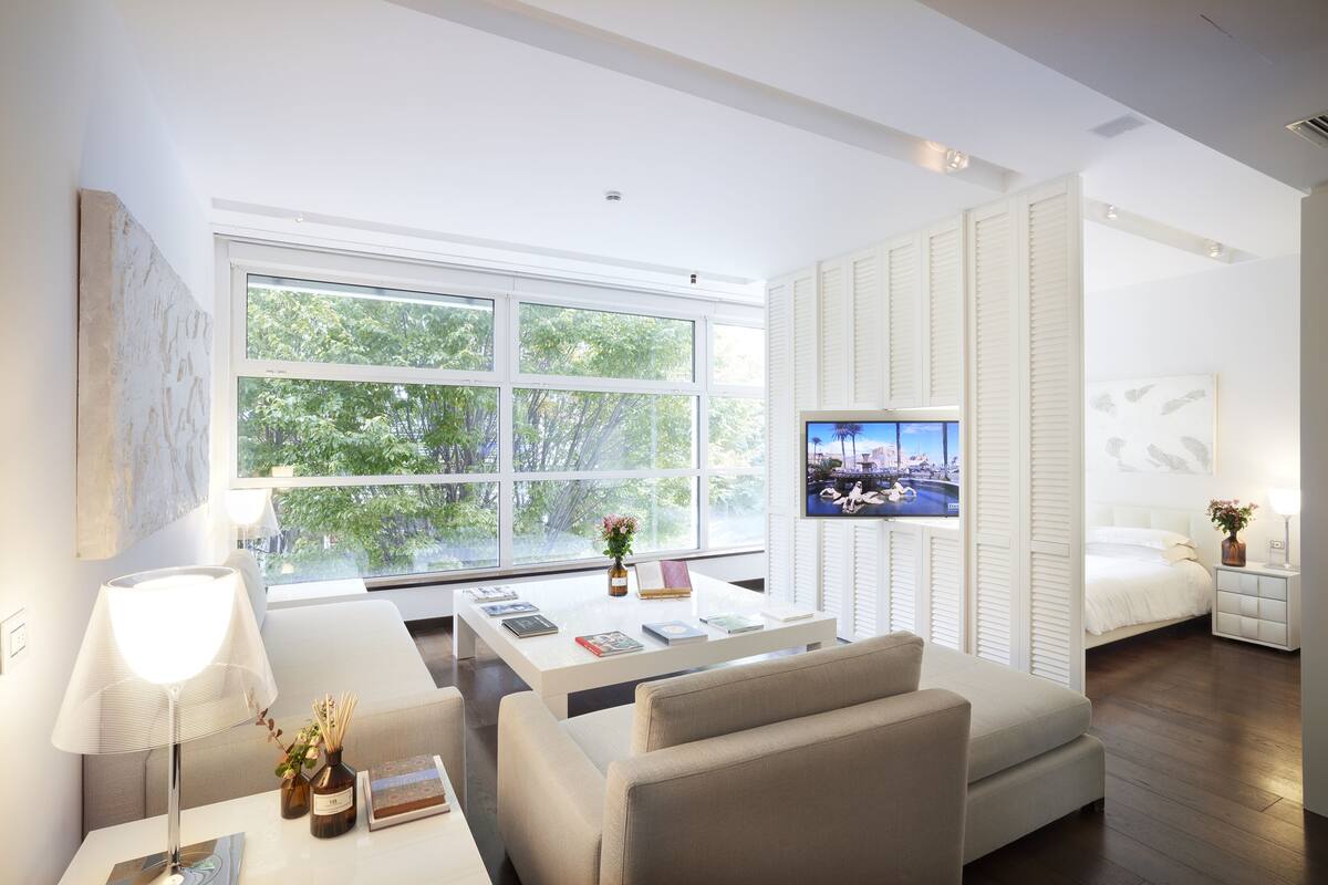 A modern hotel room with a large window, a bed, a sofa, a coffee table, and a TV.