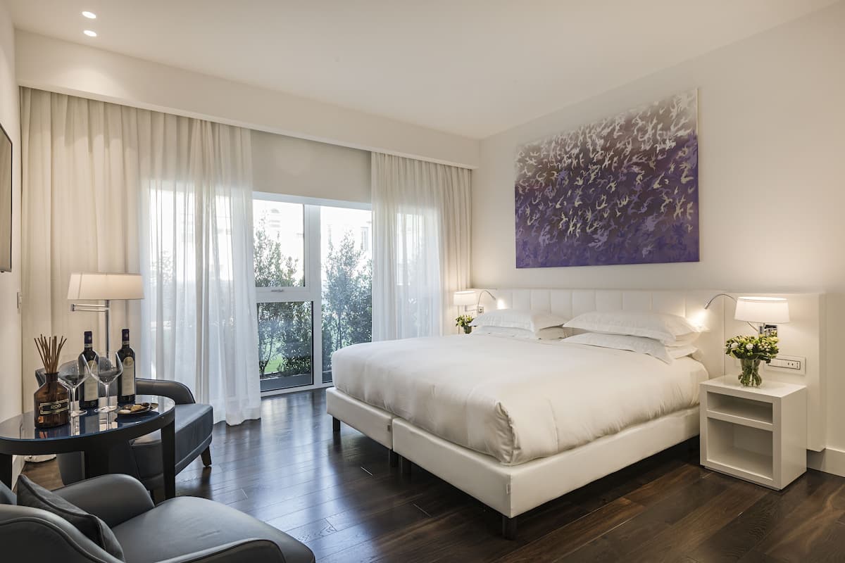 A modern bedroom with a large bed, bedside tables, a desk, and a view of the outdoors.