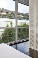Una stanza con ampie finestre, pavimento in legno e vista su edifici e alberi.