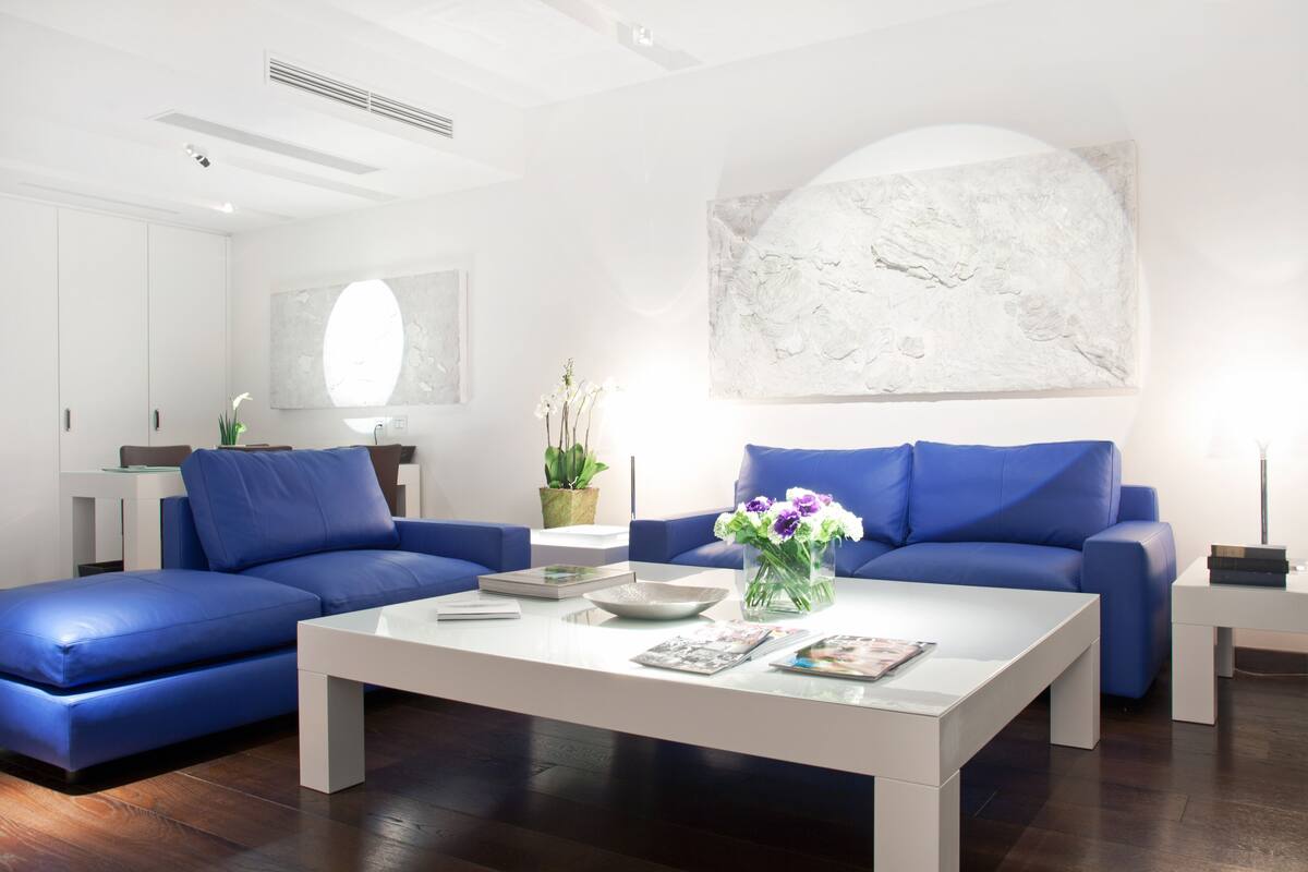 A modern living room with a blue sofa, a white coffee table, and a large abstract painting on the wall.