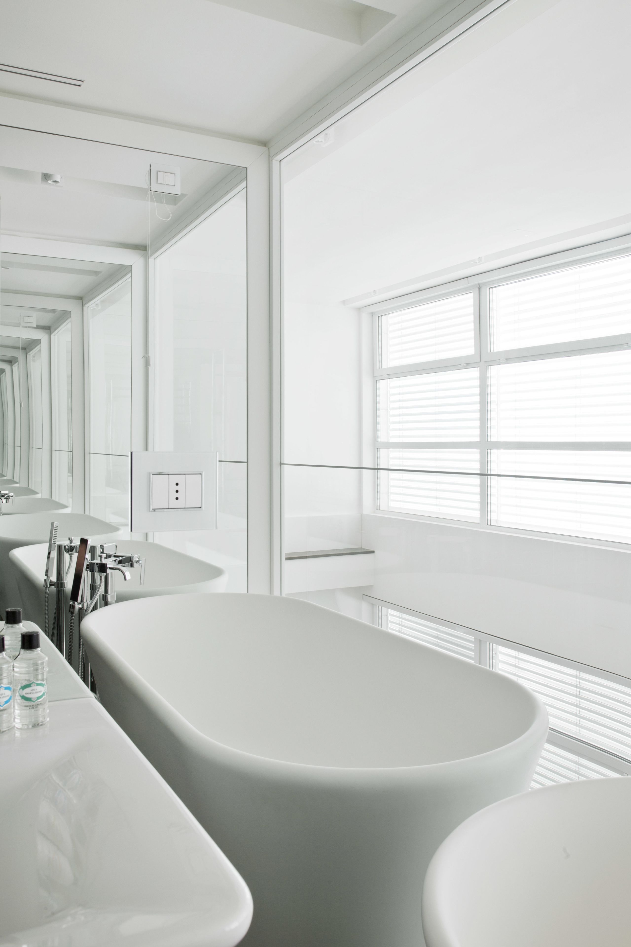 Ein modernes Badezimmer mit einer großen Badewanne, einem Spiegel und einem Fenster mit Jalousien.