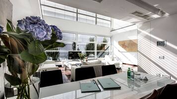 A modern meeting room with a glass table, white walls, and large windows allowing natural light.