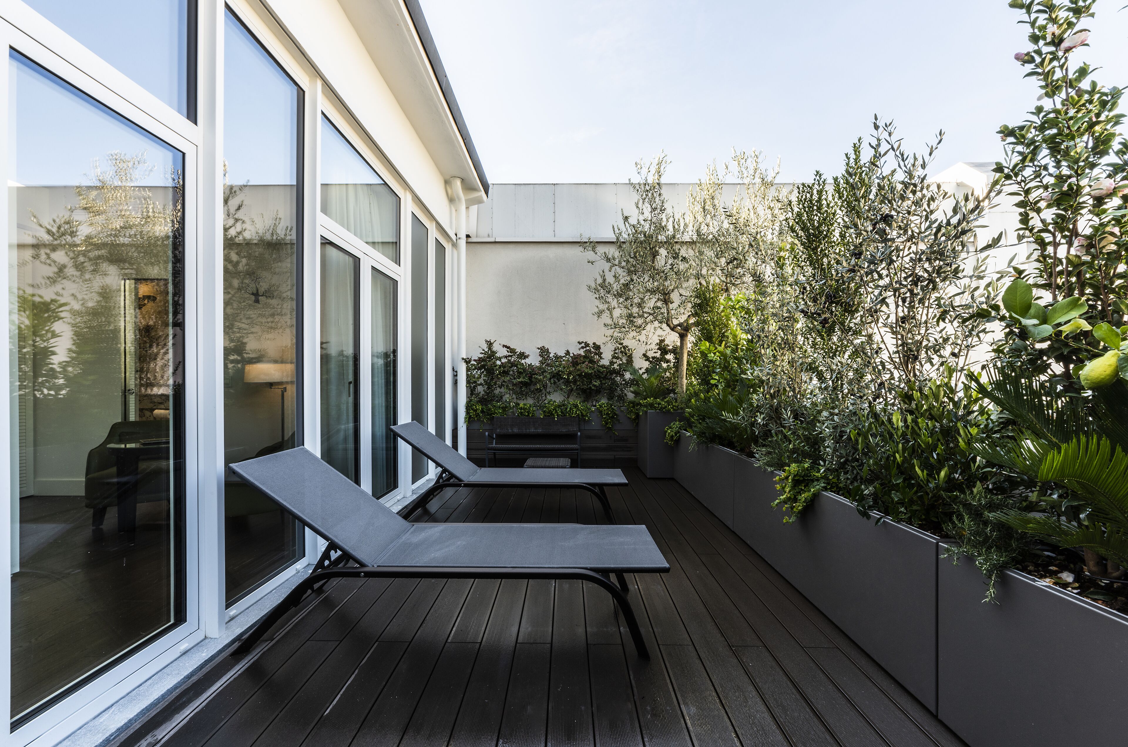 Een modern terras buiten met twee lounge fauteuils, een houten terras en een plantenwand met diverse planten.