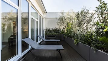 Een modern terras buiten met twee lounge fauteuils, een houten terras en een plantenwand met diverse planten.